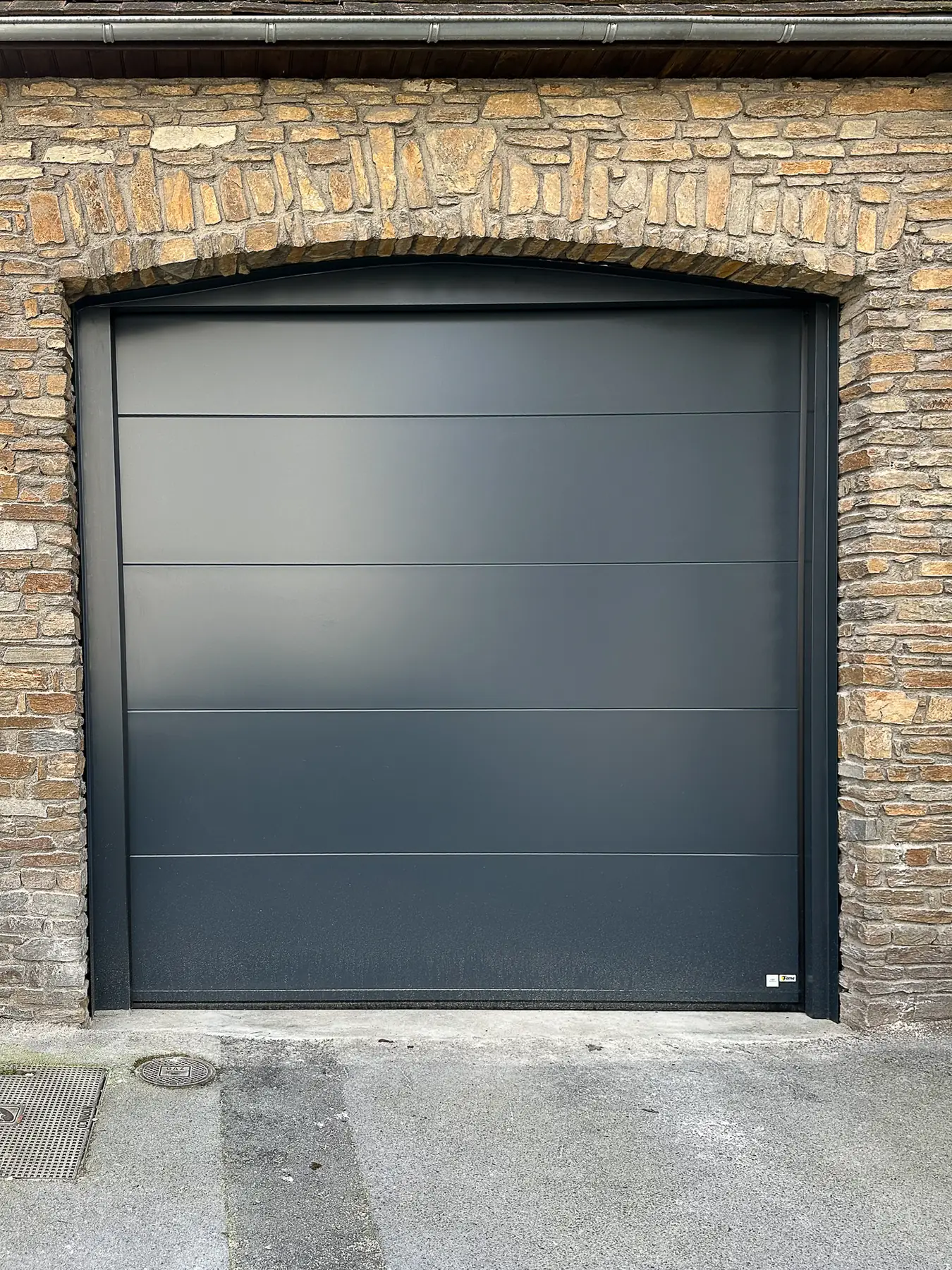Porte de garage sectionnelle anthracite dans une façade en pierre à Reims